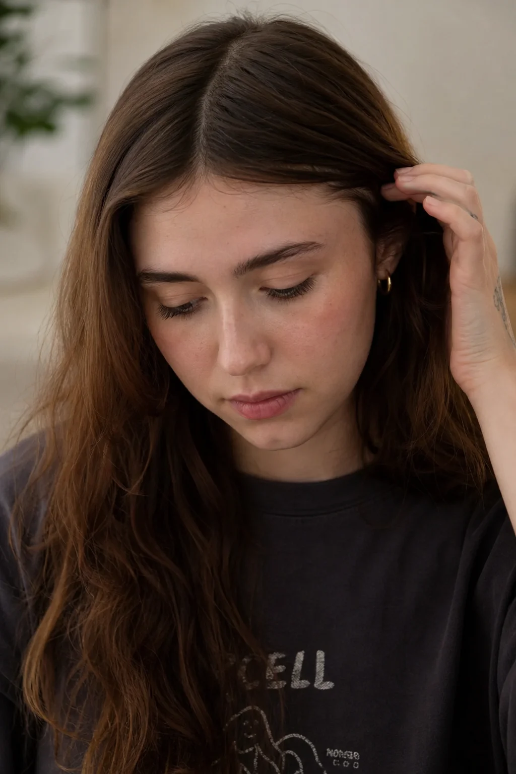 A realistic close-up portrait of singer Clairo looking downward with a subtly abashed expression, tucking a strand of hair behind her ear in soft natural light.